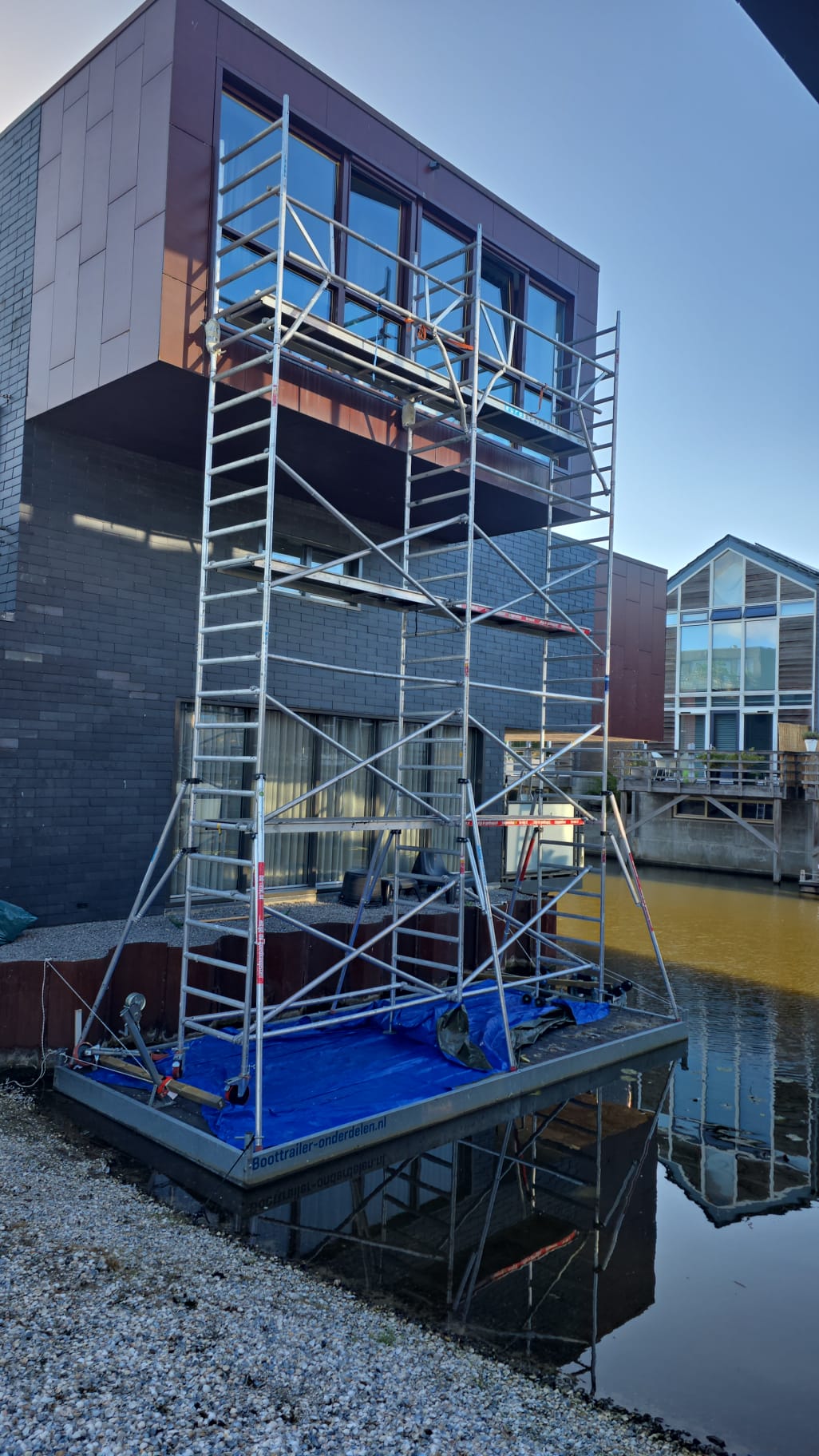 Rolsteiger op een ponton voor buitenschilderwerk aan kozijnen van een woning aan het water