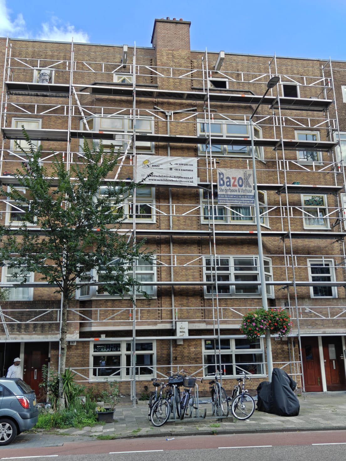 Steiger met spandoek van Schildersbedrijf Benzz tegen een portiekflat in Amsterdam voor buitenschilderwerk